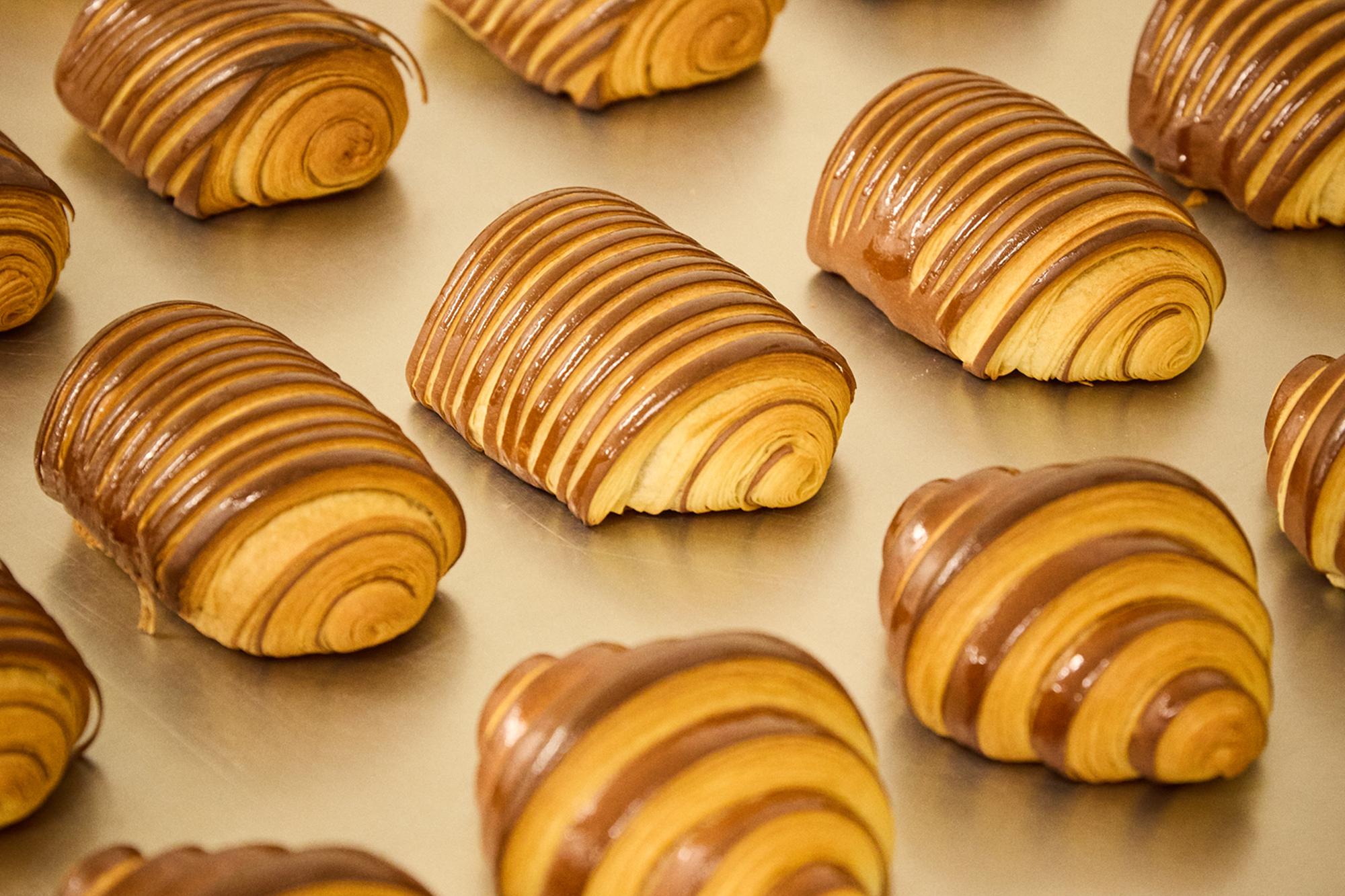 Rangées de pains au chocolat brillants sur plaque en sortie de four.